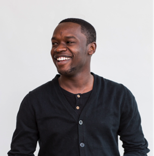 A man with short hair is smiling and looking slightly to the side. He is wearing a black cardigan over a black shirt against a plain white background.